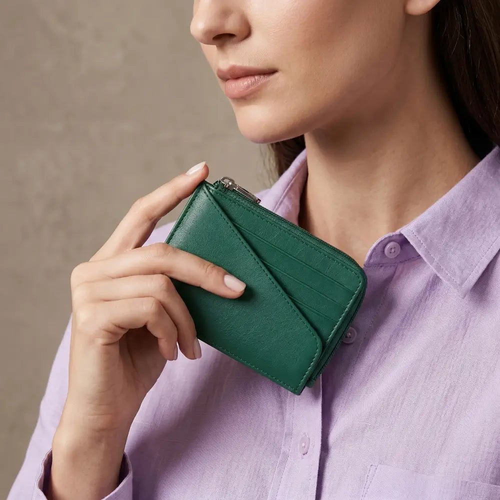 Woman holding a green wallet against a neutral background