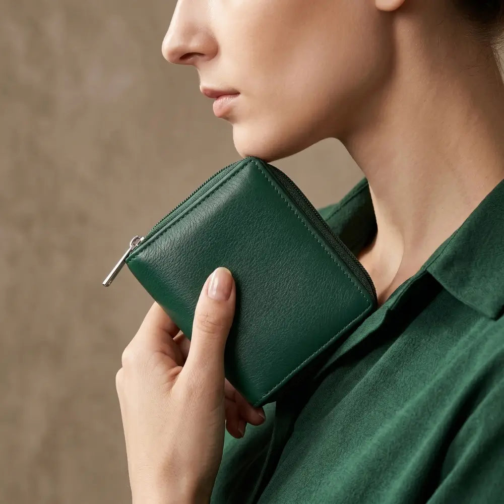 Person holding a green leather wallet against a neutral background