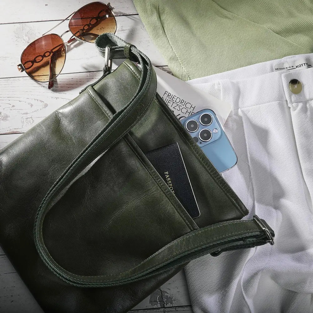 Green leather bag with sunglasses, phone, and book on a wooden surface