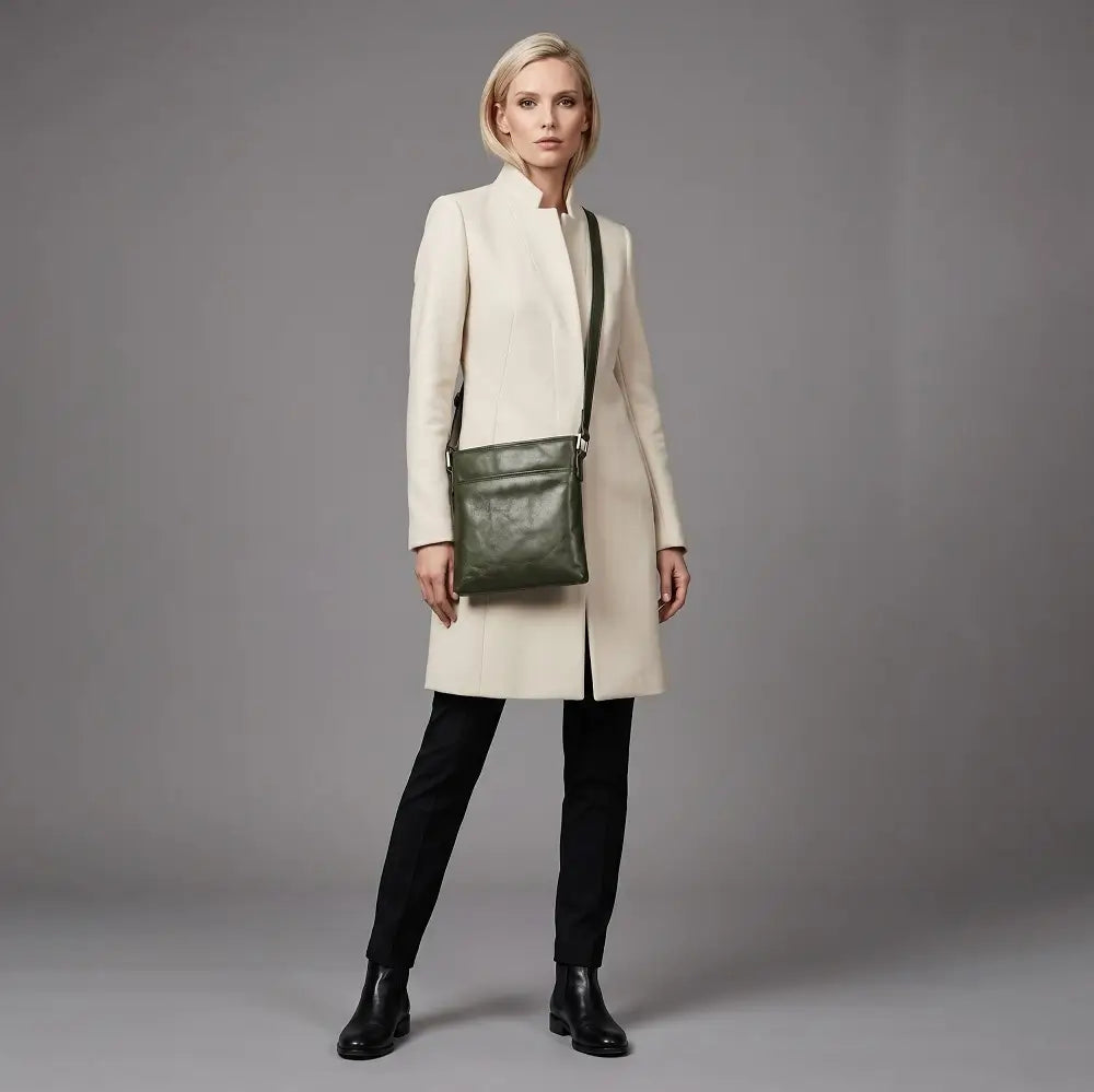 Woman wearing a long beige coat holding a green leather bag against a gray background