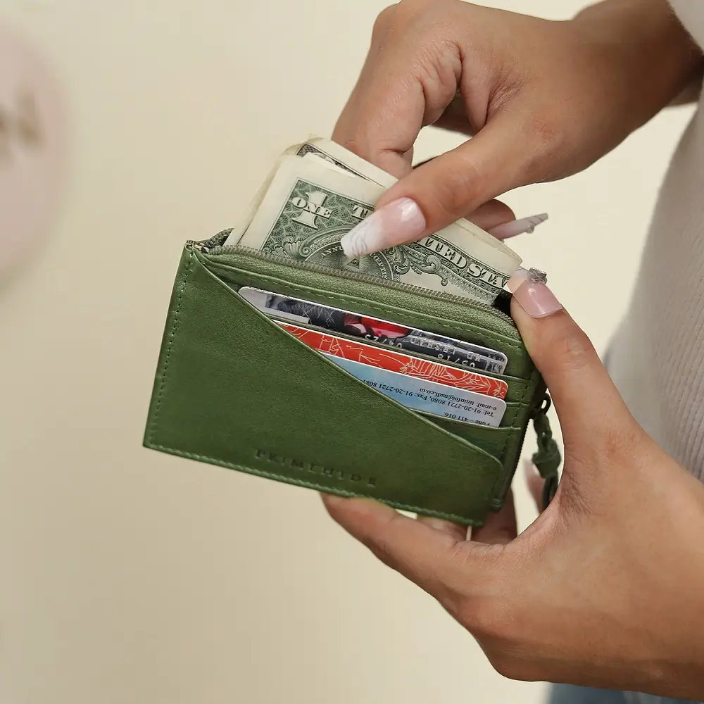 Green wallet with money and cards held by a person against a neutral background