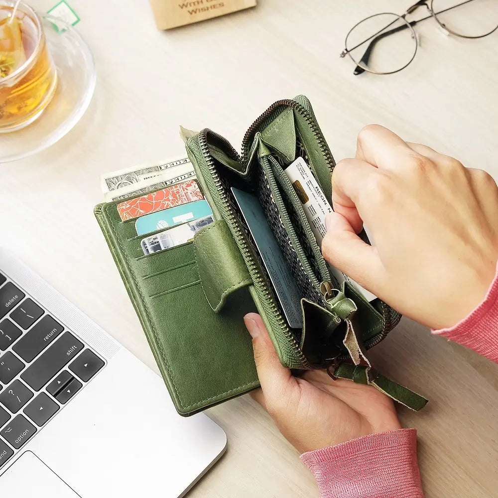 Green wallet with cards and money held by a hand on a desk with a laptop and tea.