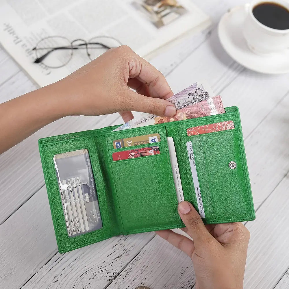 Green wallet with money and cards on a wooden surface with a cup of coffee and glasses in the background.