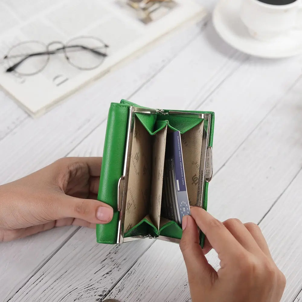 Green wallet with card slots held by a hand on a light wooden surface.