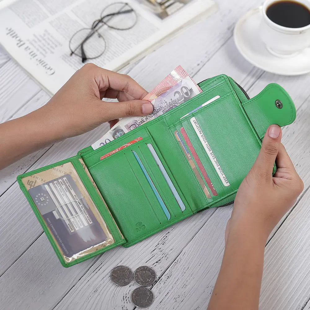 Green wallet with money and cards on a wooden surface with a cup of coffee and glasses.