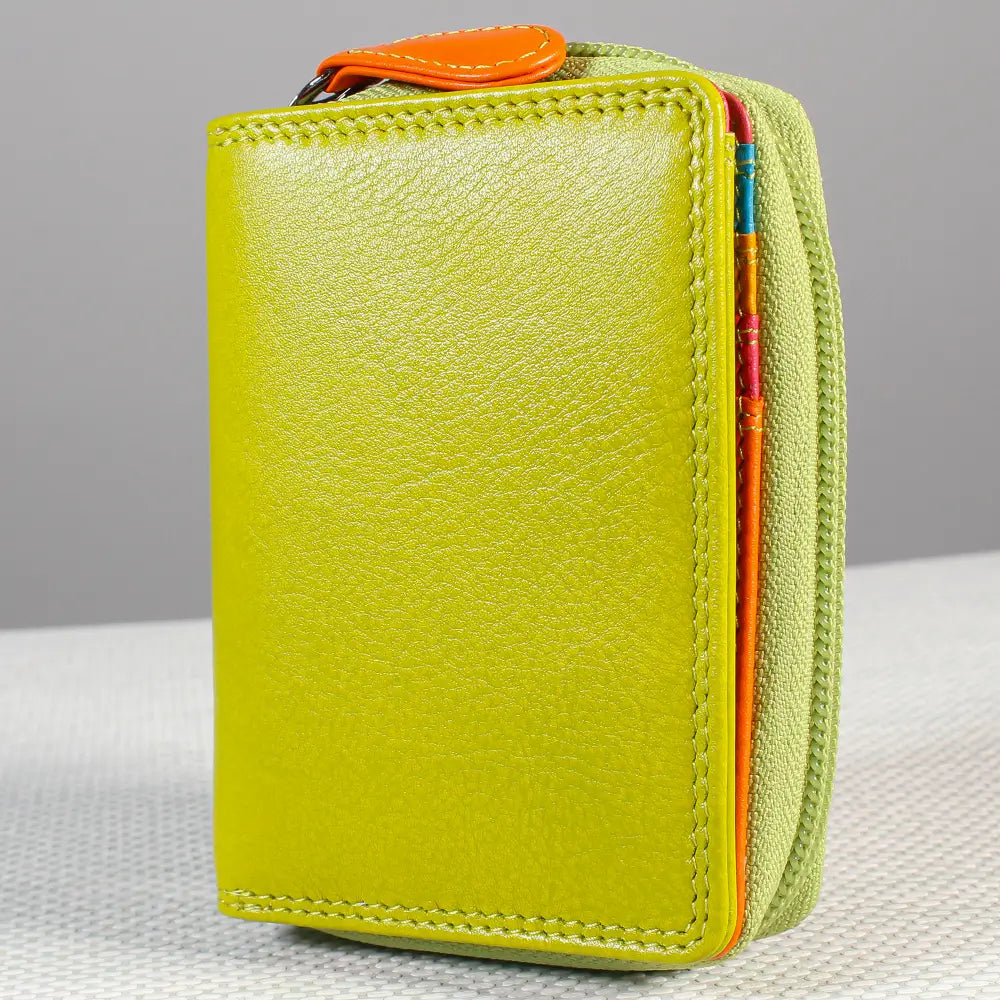 A green textured leather zip-around card holder wallet with an orange zipper pull, standing upright on a light textured surface against a neutral gray background.