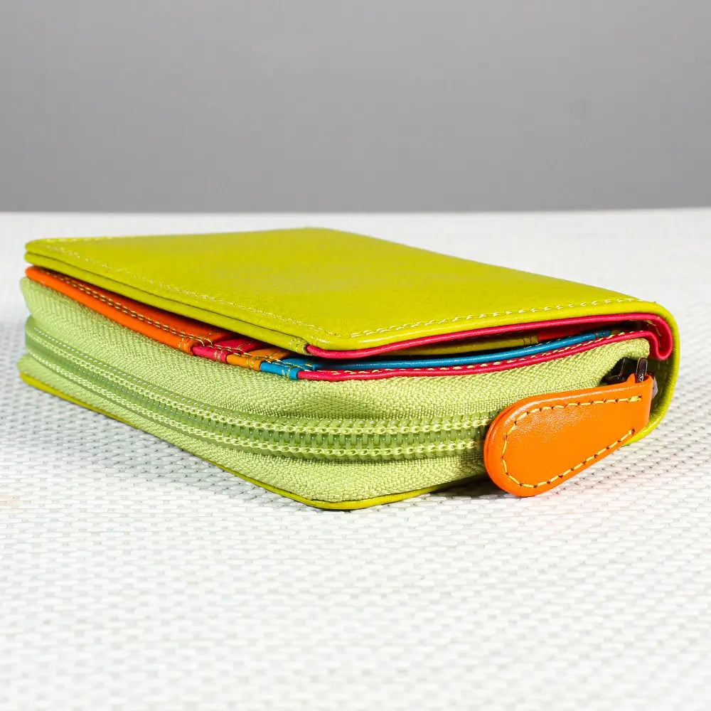 A green zippered wallet or card holder with an orange leather pull tab, shown on a white textured surface against a gray background.