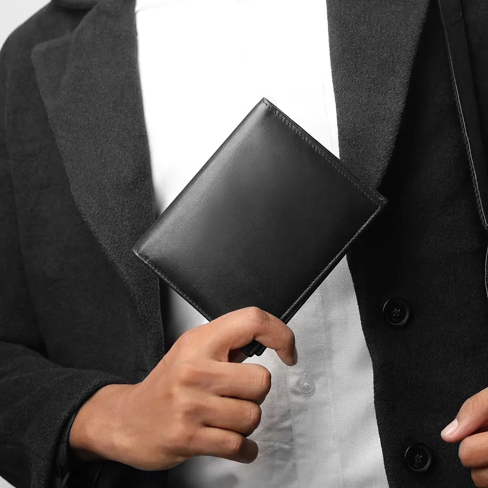 Person holding a black leather wallet against a neutral background