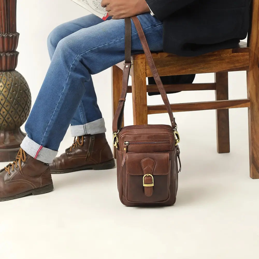 Brown leather crossbody messenger bag worn casually with jeans, showing compact size and adjustable shoulder strap.