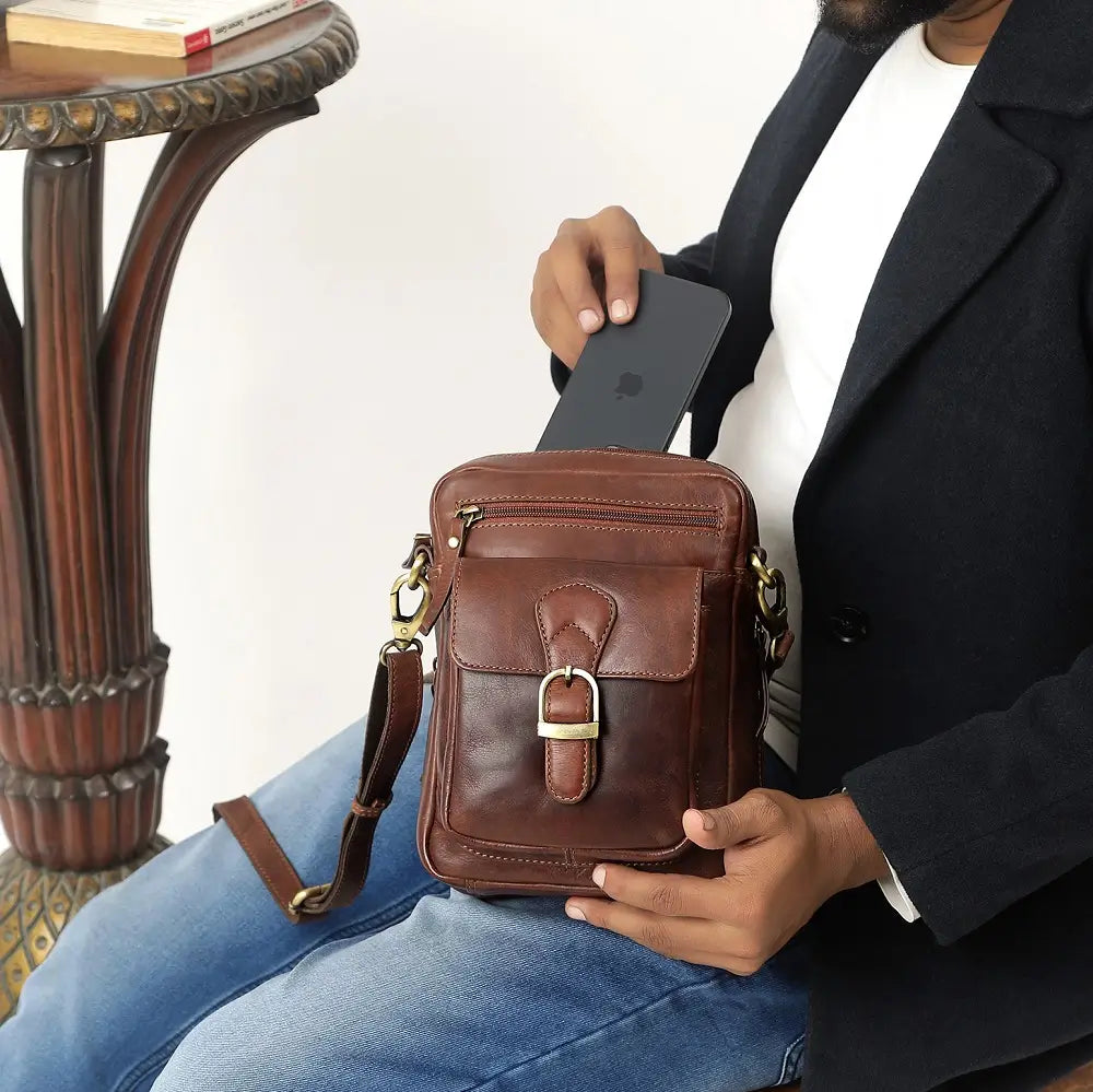 Leather crossbody messenger bag in brown with front flap pocket, showing easy access to smartphone storage