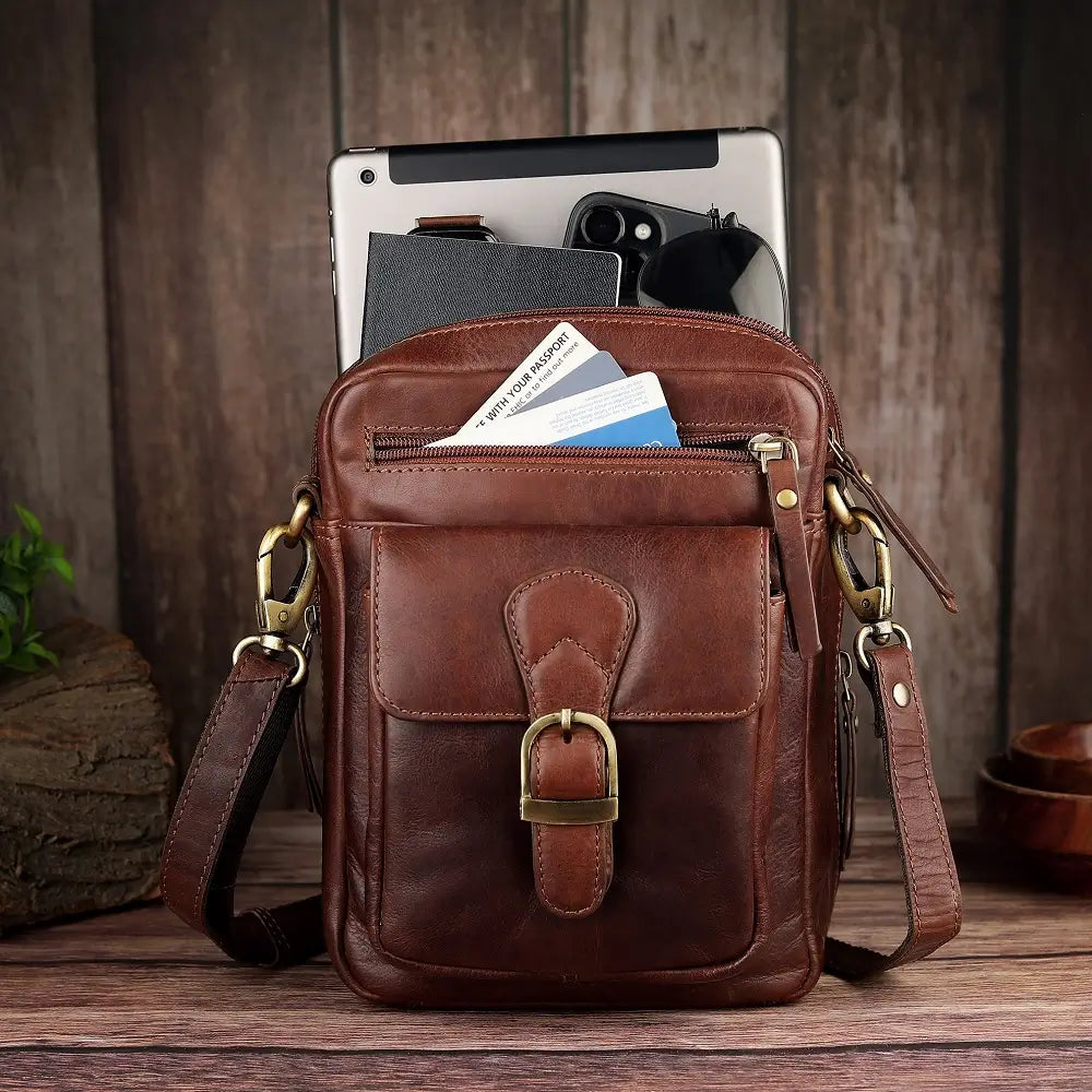 Brown leather crossbody bag with compartments on a wooden surface