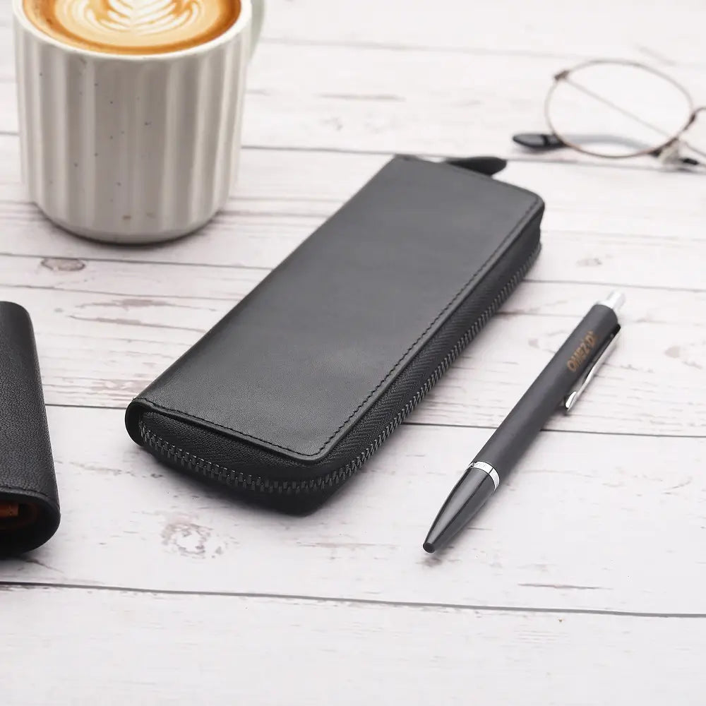 Black leather wallet, pen, and glasses on a wooden surface with a cup of coffee.