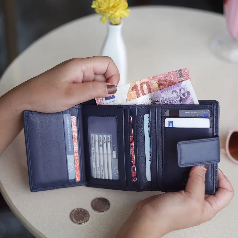 Person holding soft navy leather trifold purse with secure tab fastening
