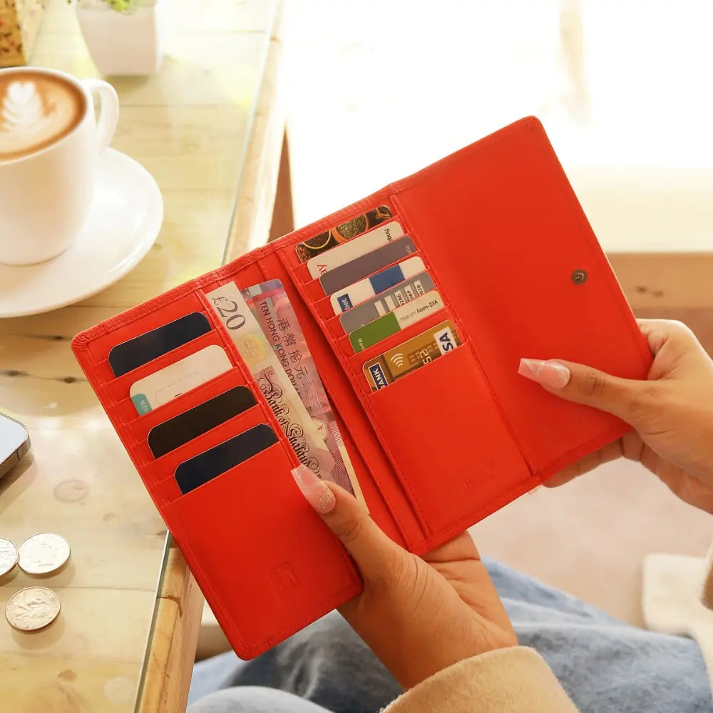 Orange  wallet with card slots and cash held by a hand, with a blurred background of a cafe setting.