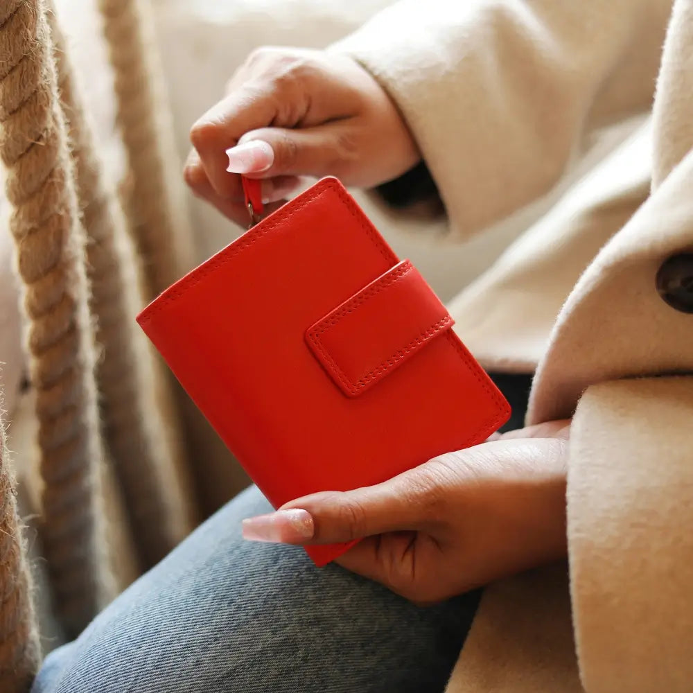 Person holding soft orange leather trifold purse with secure tab fastening