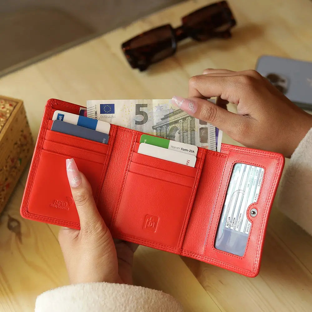 Orange wallet with money and cards held by a person on a wooden surface.