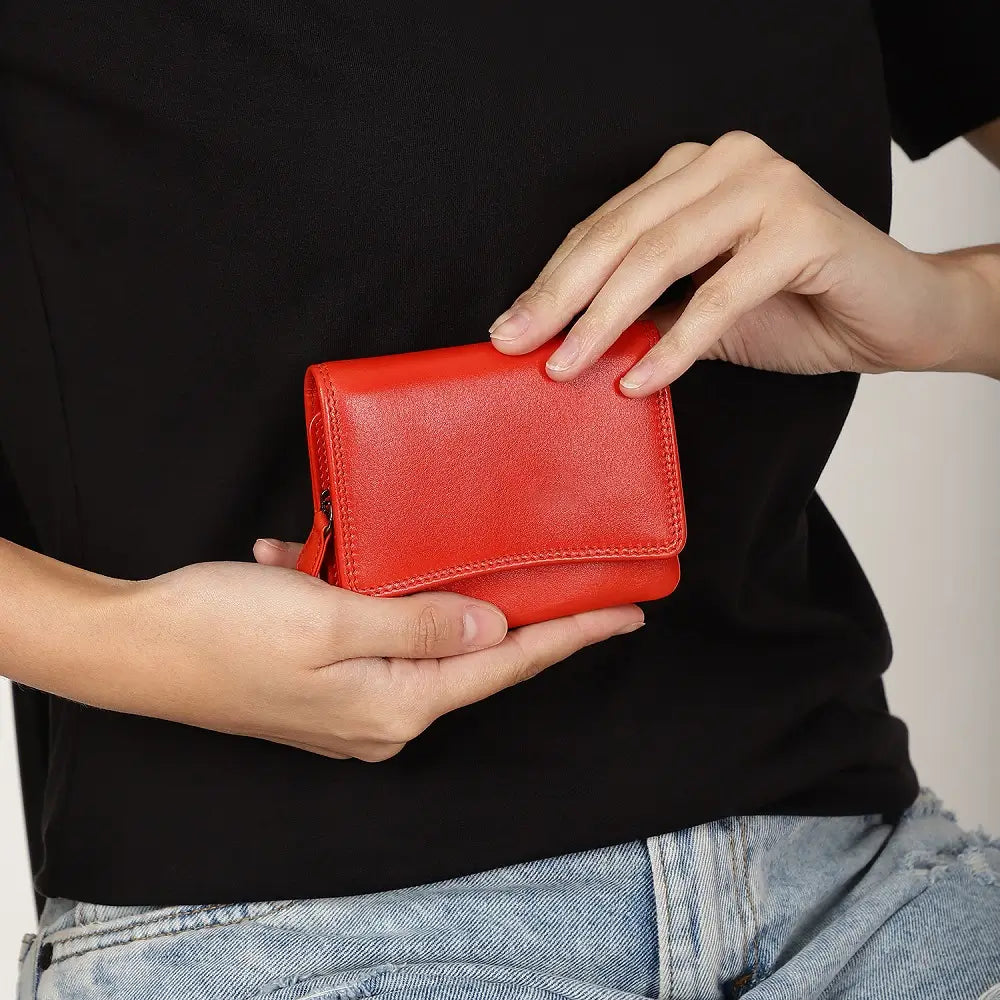 Person holding a orange wallet against a black shirt and light blue jeans.