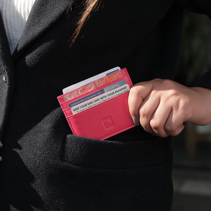 Red leather card holder with cash and cards on a white desk with accessories