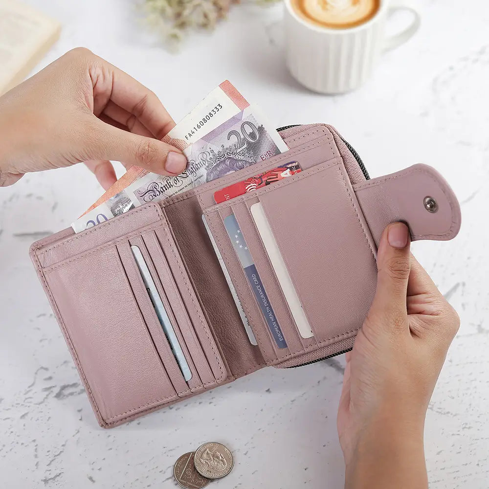 Pink wallet with cards and money held by hands on a light surface with a blurred coffee cup in the background