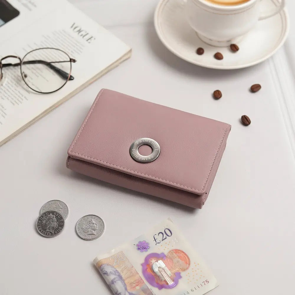 Pink wallet with coins and banknotes on a table with a cup of coffee and glasses.