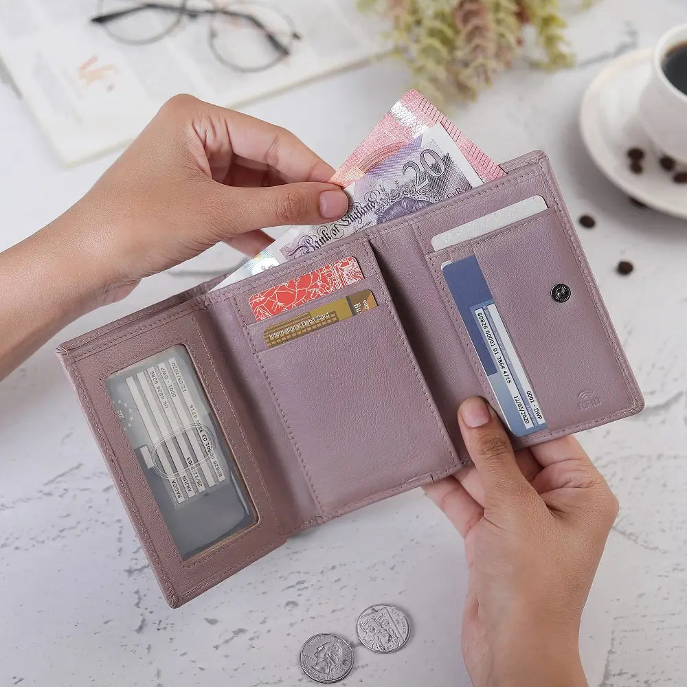 Person holding a pink wallet with money and cards on a light surface.