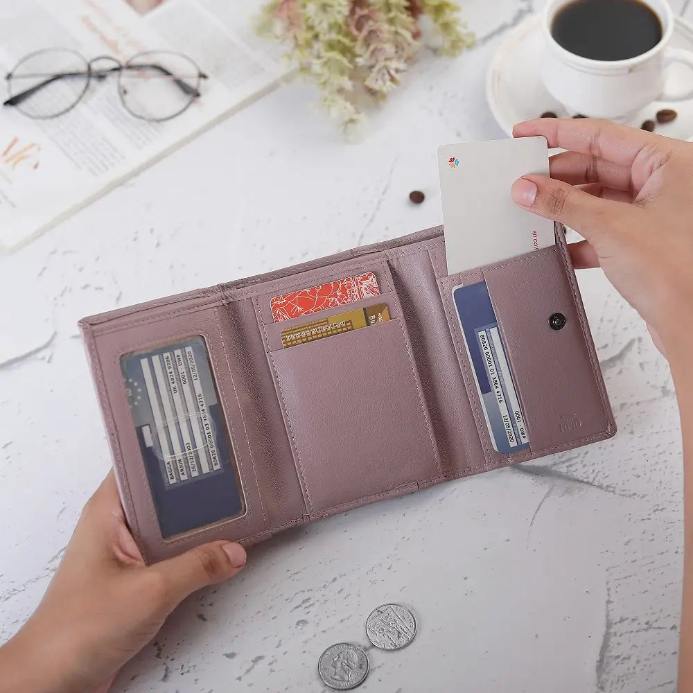 Person holding a pink wallet with cards and coins on a white surface with a cup of coffee and glasses.