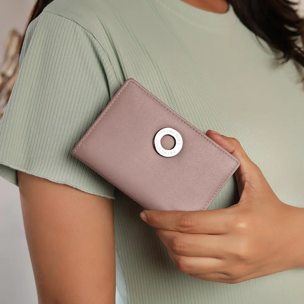 Person holding a pink wallet with a silver ring detail against a neutral background