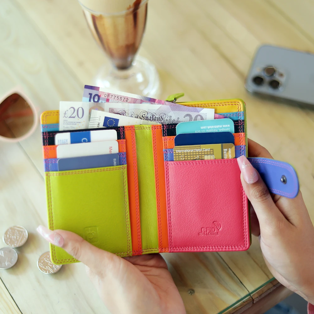 pink wallet with money and cards held by a hand on a wooden table.