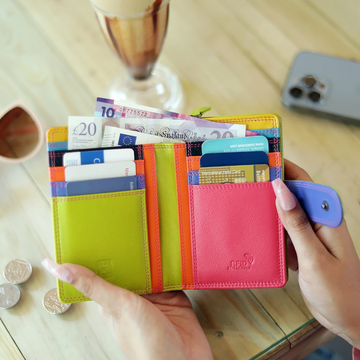 pink wallet with money and cards held by a hand on a wooden table.