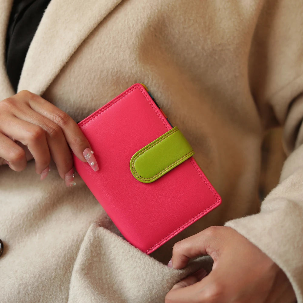 Person holding a pink purse with a green strap against a beige coat.