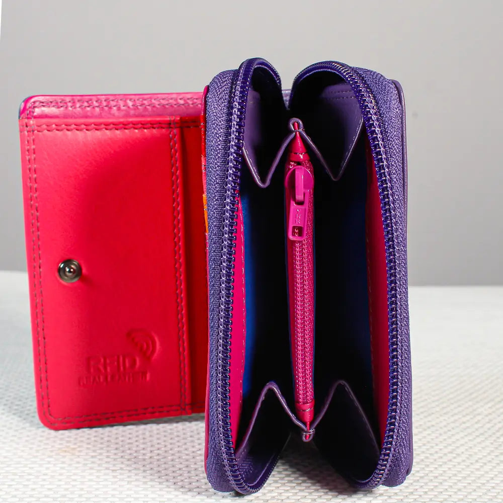 A purple textured leather zip-around wallet shown open, revealing a pink interior and card slots, with a matching closed wallet standing behind it on a light surface.