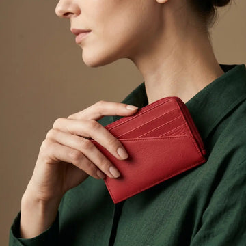 Person holding a red wallet against a neutral background