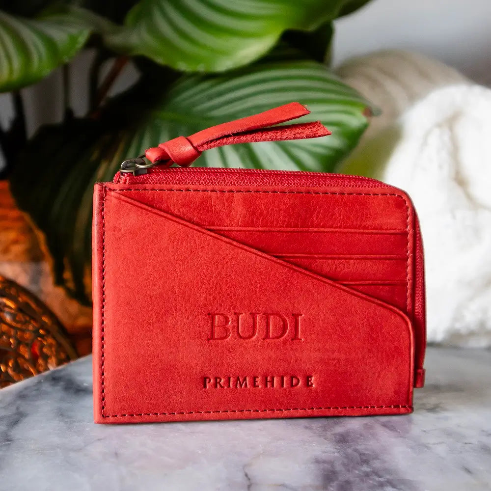 Red wallet with 'Budi' branding on a marble surface with a plant in the background