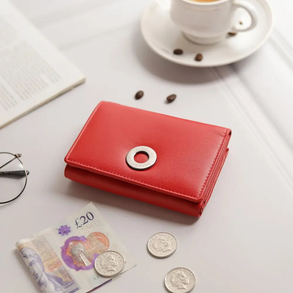 Red wallet with coins and banknotes on a table with a cup of coffee in the background