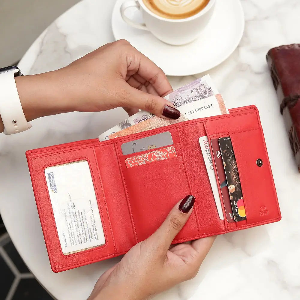 Red wallet with cards and cash held by a hand, with a cup of coffee in the background.