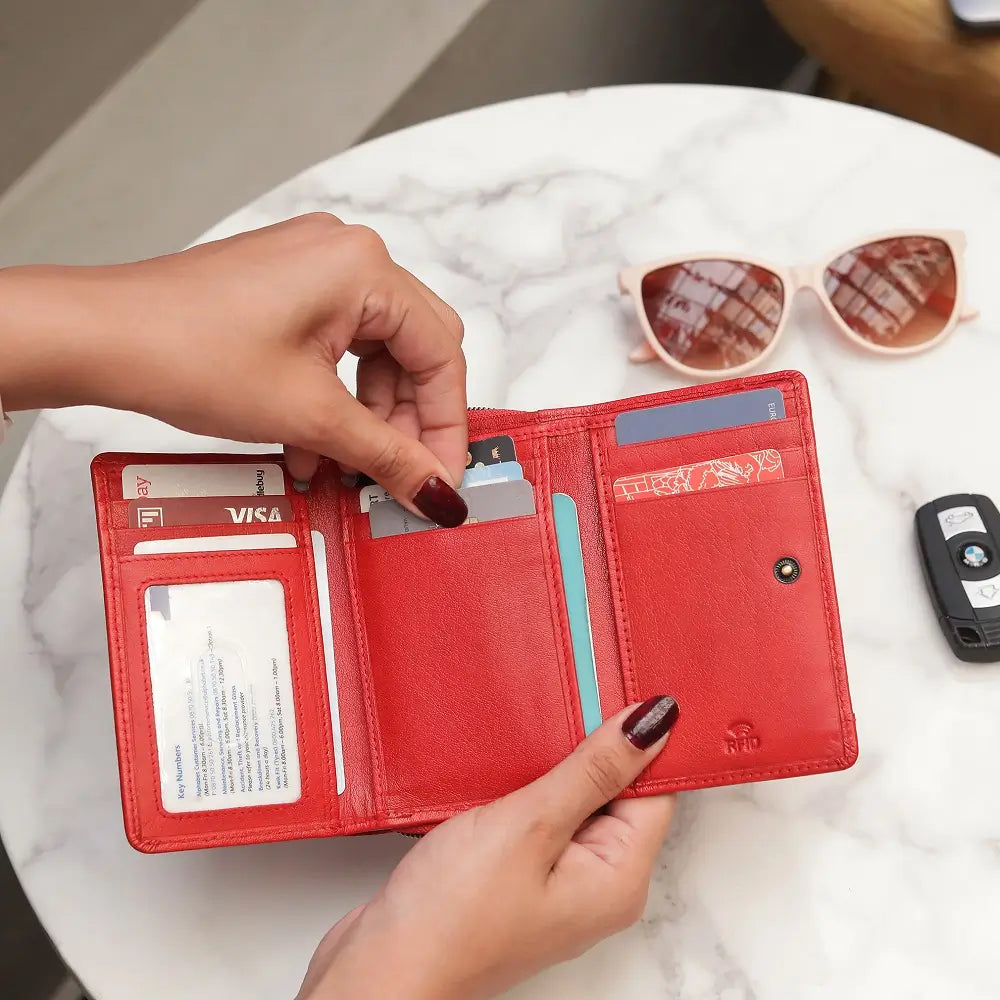 Red wallet with cards and a key fob on a marble surface
