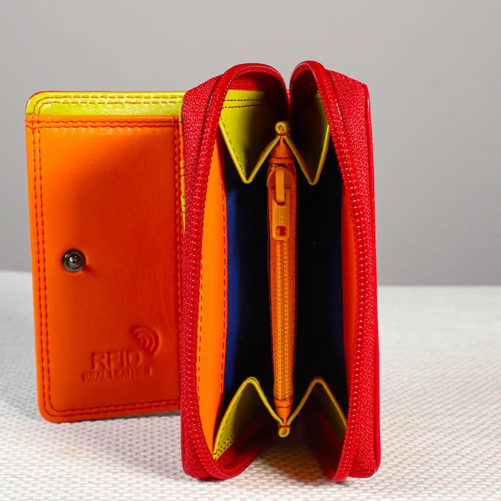 A colorful zip-around wallet shown open and closed. The wallet has a red exterior, a bright orange interior, and yellow and blue lining details, photographed on a light textured surface against a neutral gray background.