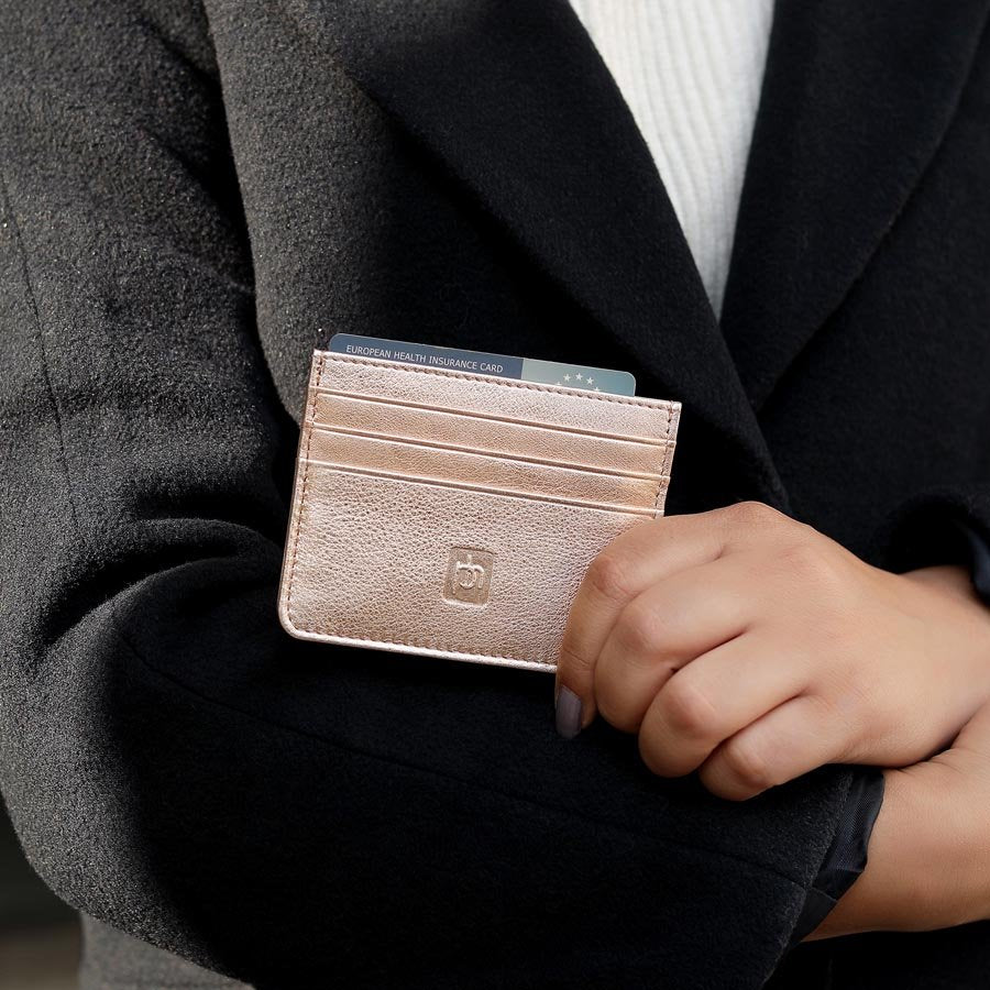 Hand holding rose gold leather card holder against a black coat, showing neatly inserted cards.