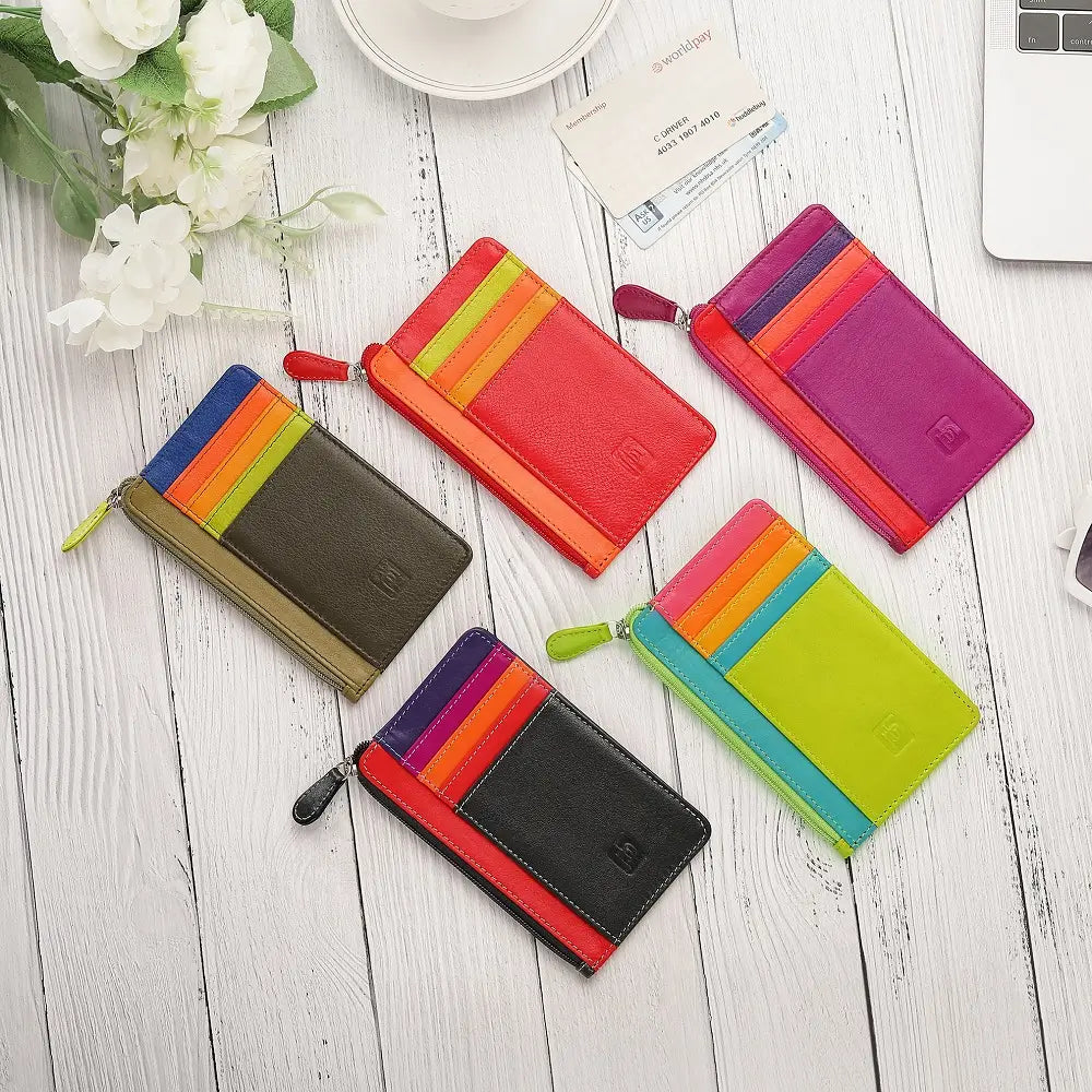 Colorful wallets on a wooden surface with flowers and a card in the background