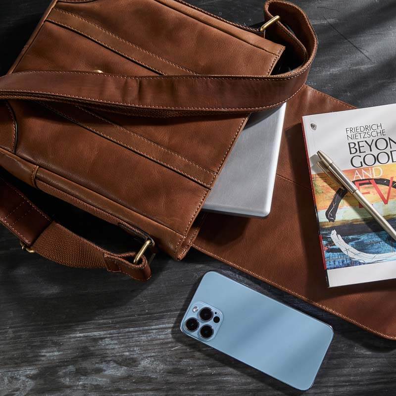 Brown leather bag with a phone, book, and pen on a dark surface