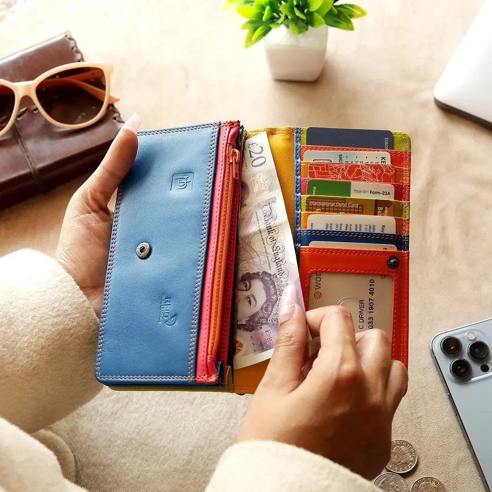 Person holding a Orange wallet with cards and money next to glasses  on a wooden table.