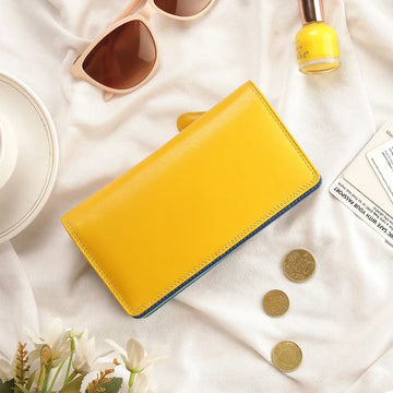 Yellow wallet on a white surface with sunglasses, coins, and a bottle of nail polish.