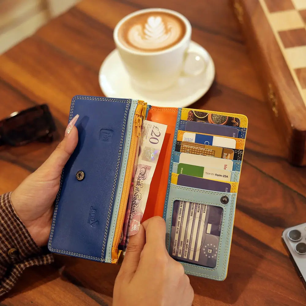 Person holding a Yellow wallet with cards and money next to a cup of coffee on a wooden table.