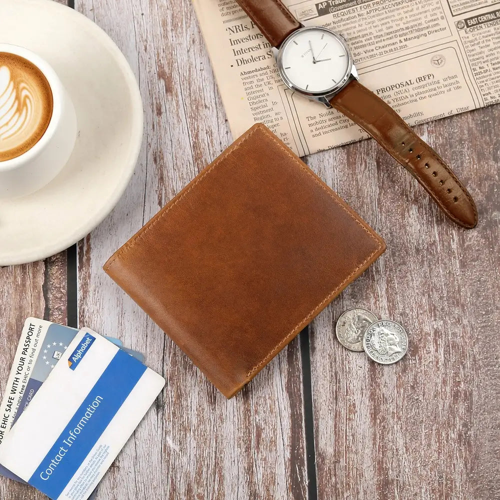 Tan leather wallet, watch, and coffee on a wooden surface with newspaper.