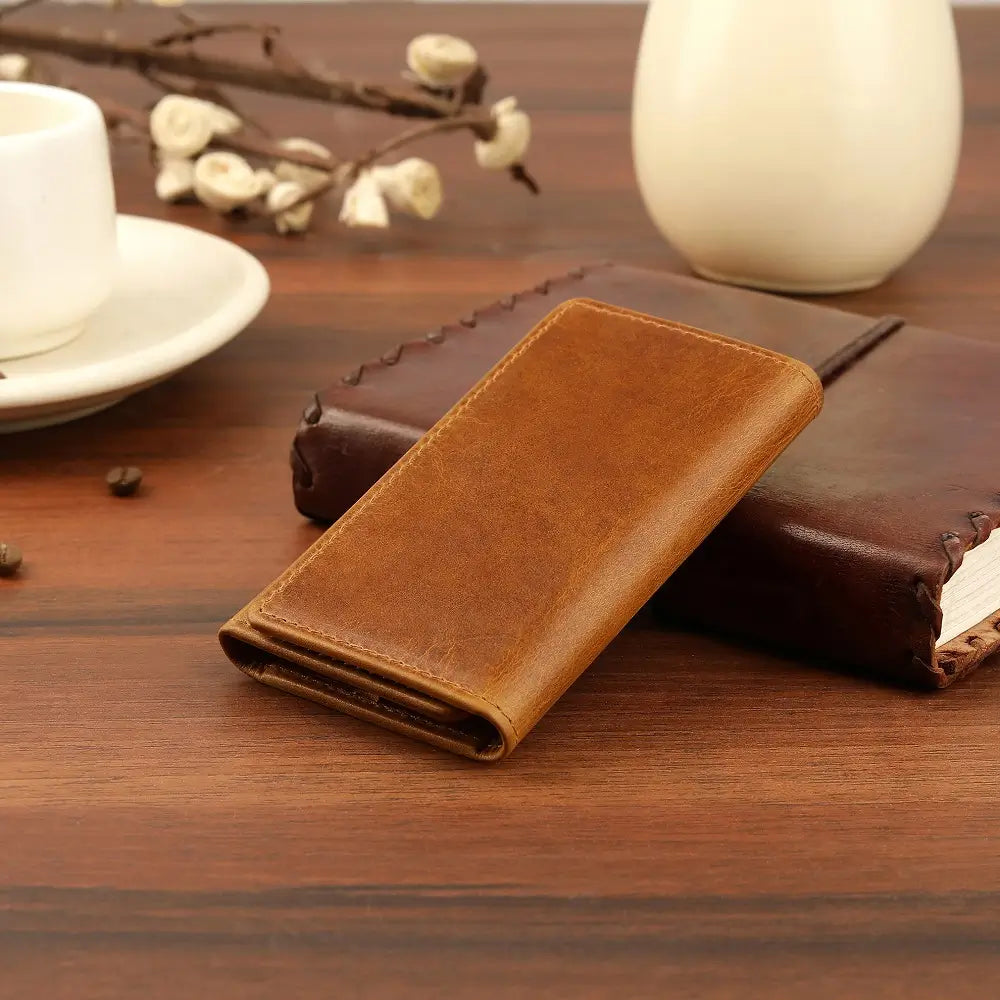 Tan leather wallet on a wooden surface with a cup and decorative elements.