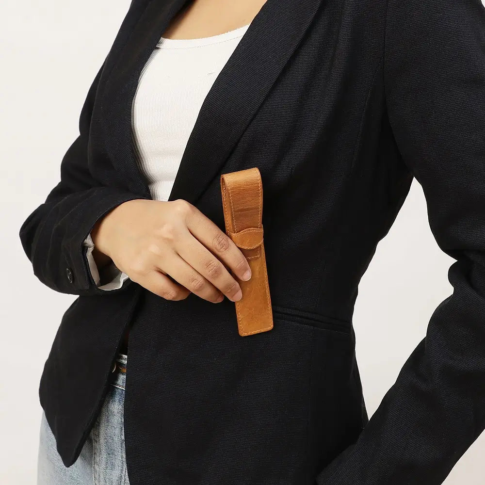 Person wearing a black blazer holding a tan leather pen holder against a light background