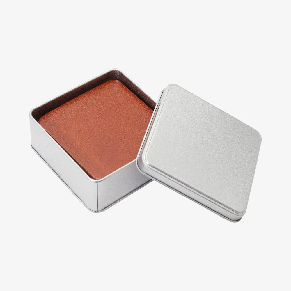 Tan leather coasters for coffee table in an open silver metal container on a white background