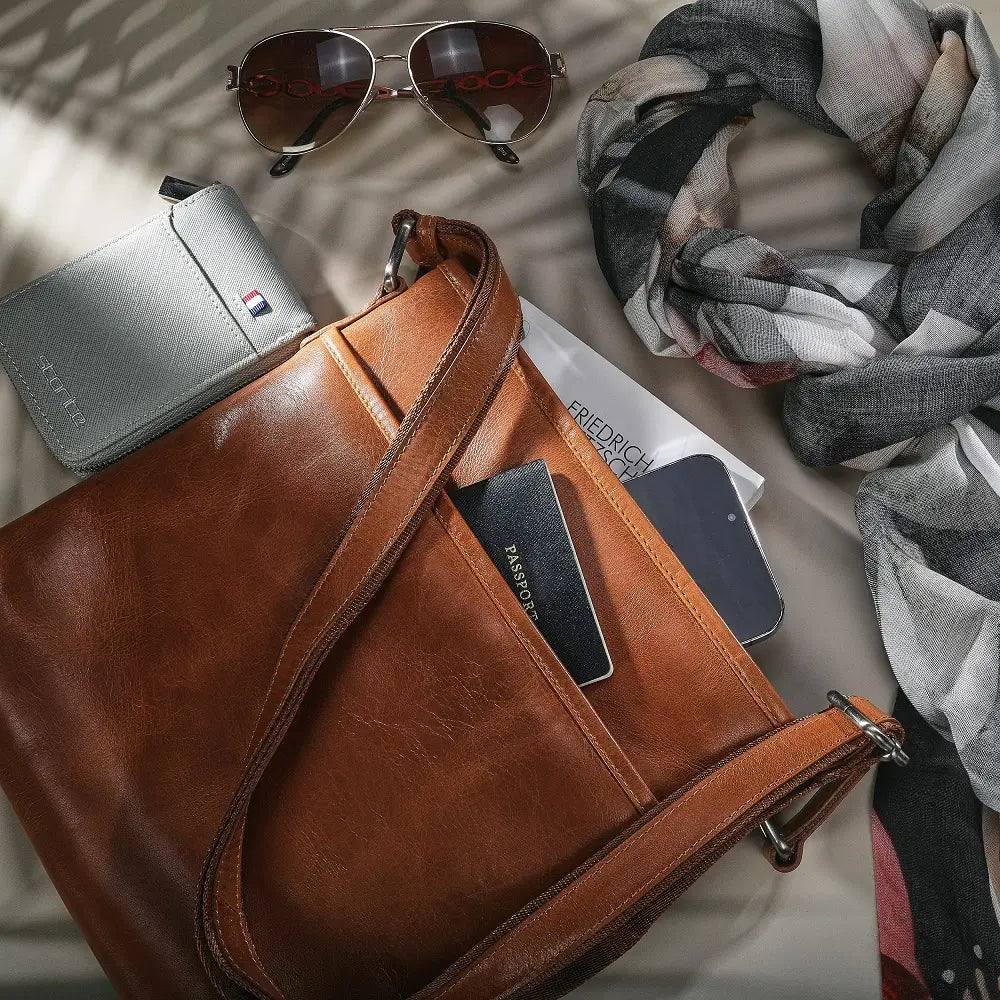 Tan leather bag with sunglasses, wallet, and phone on a light surface