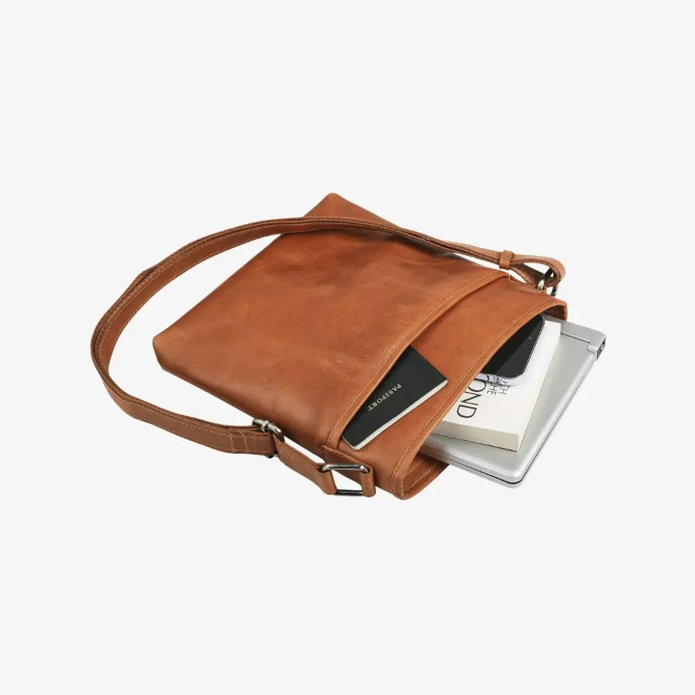 Tan leather crossbody bag with a phone and book inside on a white background