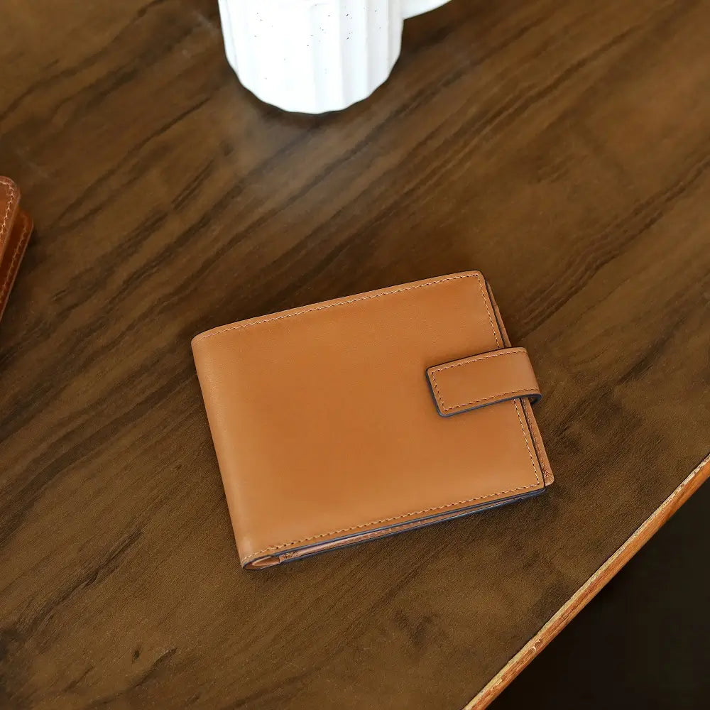 Tan leather wallet on a wooden surface with a white mug in the background